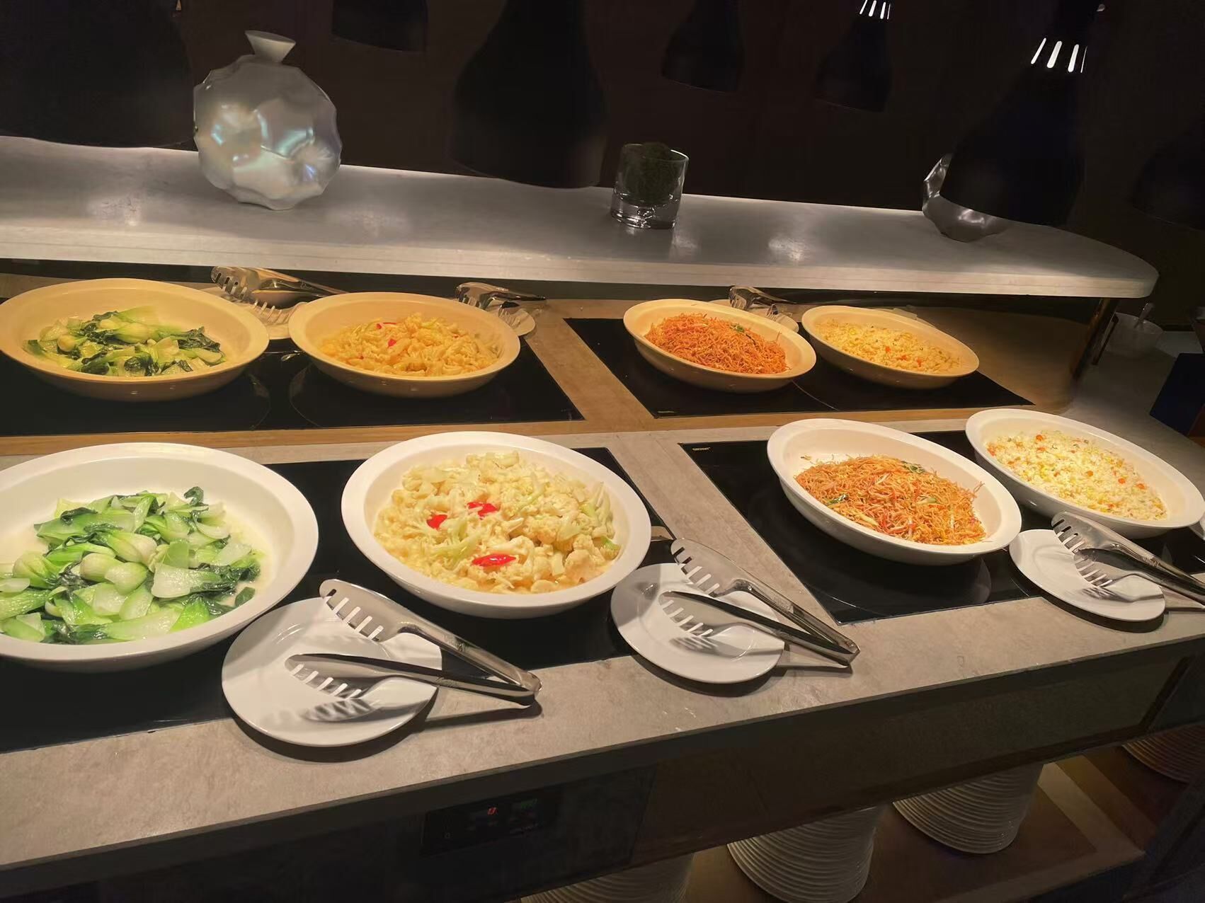 A buffet table with various dishes including vegetables, rice, and noodles.