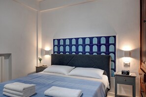 Ein Hotelzimmer mit einem Bett, zwei Nachttischen, einer Kamera auf einem Tisch und einer Wand mit geometrischem Muster.