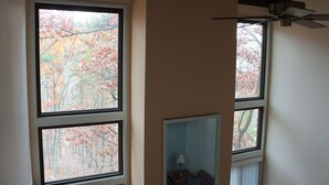 Una stanza con tre finestre, una ventola a soffitto e un tavolino con una lampada.