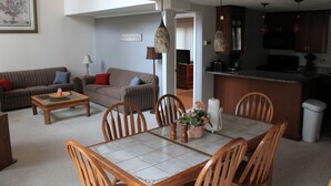 Un soggiorno con divano, tavolino e tavolo da pranzo con sedie. È presente una zona cucina con mobili e piano di lavoro.