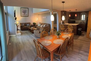 A spacious living area with a wooden dining table, multiple sofas, and a kitchen in the background. - Welcome To "Snowed Inn” - Walk On And Off The Slopes (McGaheysville)