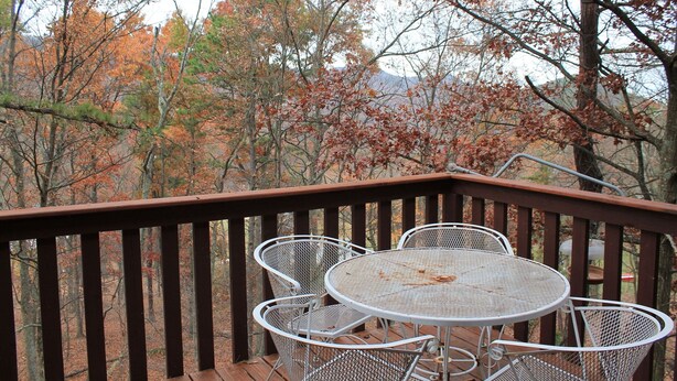 Un patio in legno con tavolo e sedie in metallo, immerso tra alberi con foglie autunnali.