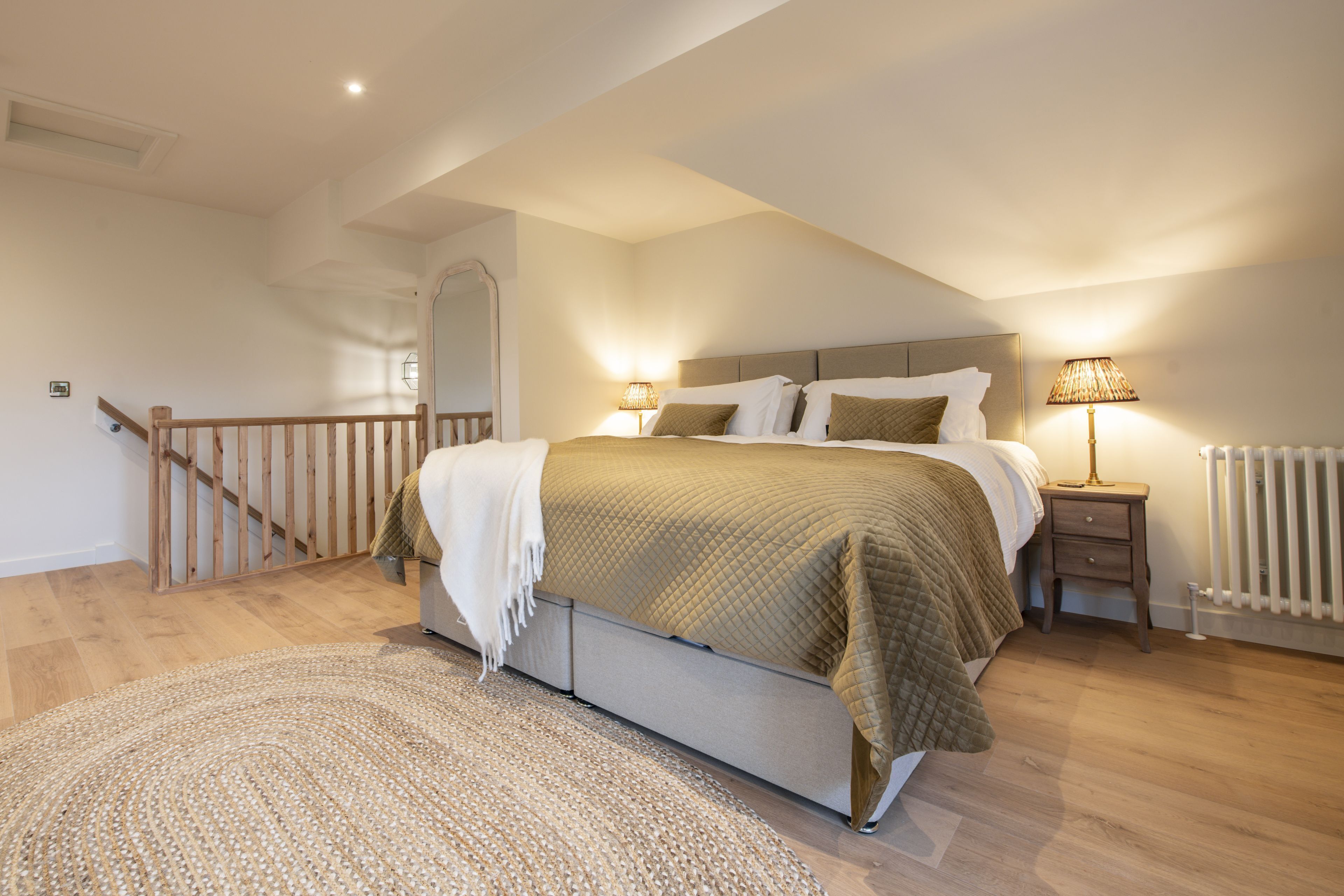 A spacious bedroom with a large bed, a wooden staircase, and a nightstand with a lamp.