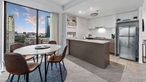 A modern kitchen with a large island, a dining area with chairs, and a view of a cityscape through large windows.