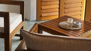 A wooden-framed room with a cushioned bench, a small table with a woven placemat, and a wooden partition. - Marshmallow Bay (Ahangama)
