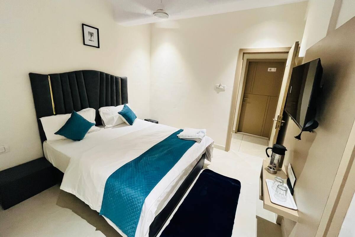 A hotel room with a bed, bedside table, TV, and a door leading to another room.