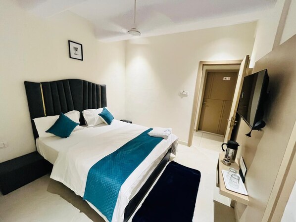 A hotel room with a bed, bedside table, TV, and a door leading to another room. - Hotel Royal SKY (Morbi)