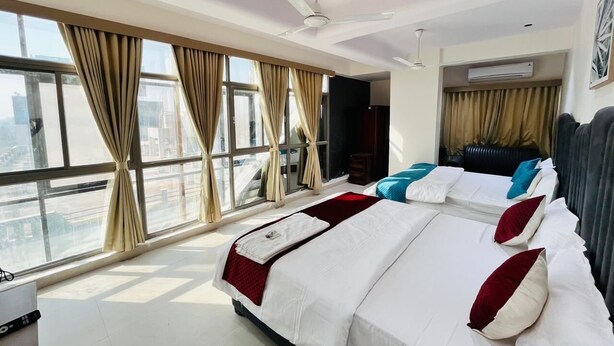 A hotel room with two beds, large windows, a ceiling fan, and an air conditioning unit. - Hotel Royal SKY (Morbi)