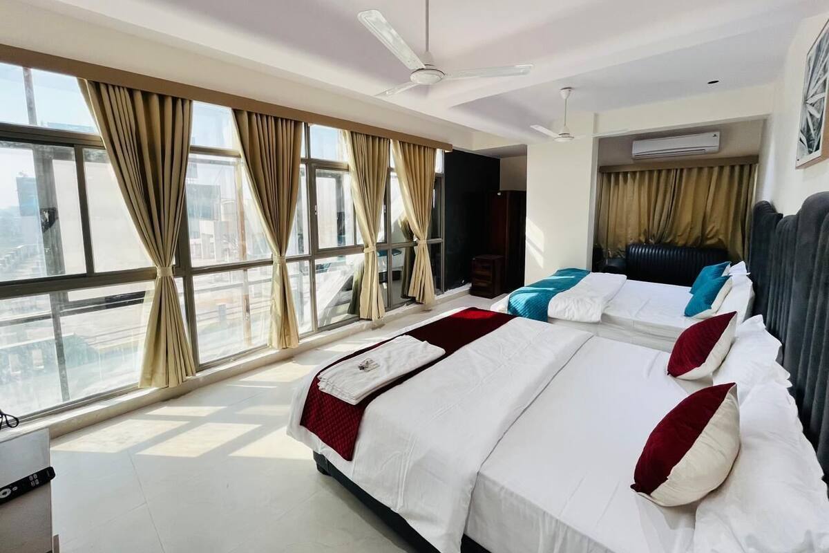 A hotel room with two beds, large windows, a ceiling fan, and an air conditioning unit.