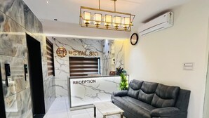 A reception area with a marble wall, a reception desk, a leather sofa, and a small table. - Hotel Royal SKY (Morbi)
