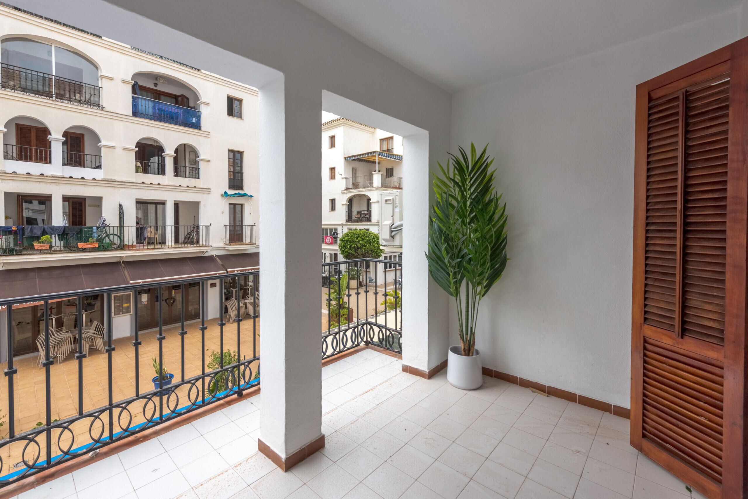 Un balcon orné d’un pot de fleurs, une vue sur un immeuble doté de balcons et un sol carrelé.