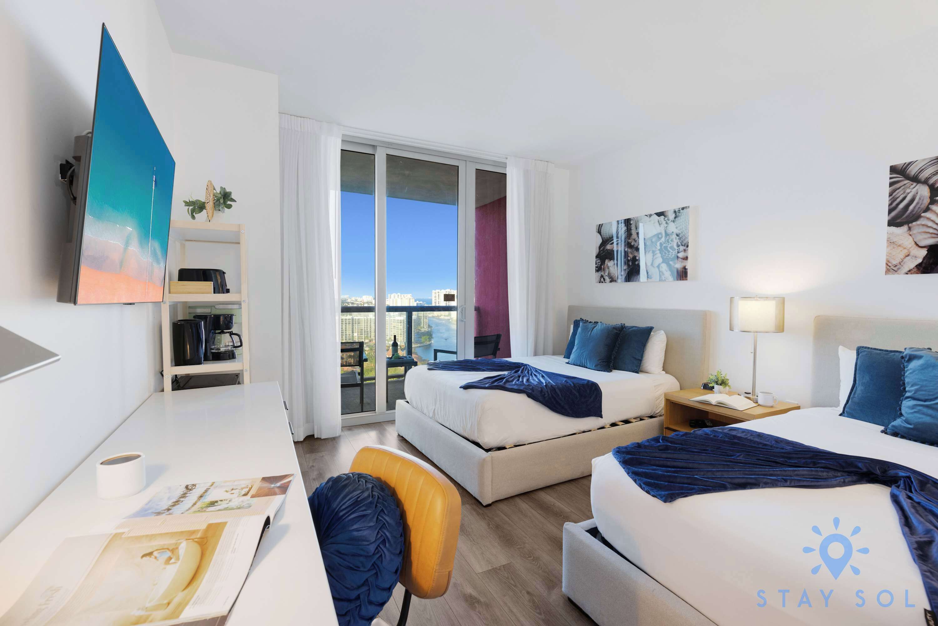 Une chambre d’hôtel avec deux lits, un bureau, une chaise, une télévision, une bibliothèque et une vue sur la ville.