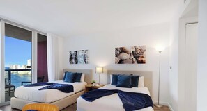Habitación de hotel con dos camas, un balcón y vista a la ciudad, además de obras de arte en las paredes.