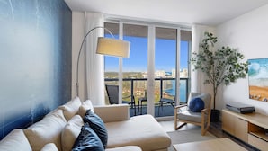 Ein modernes Wohnzimmer mit einer Couch, einer Lampe, einem Fernseher und einem Balkon mit Blick auf die Stadt.