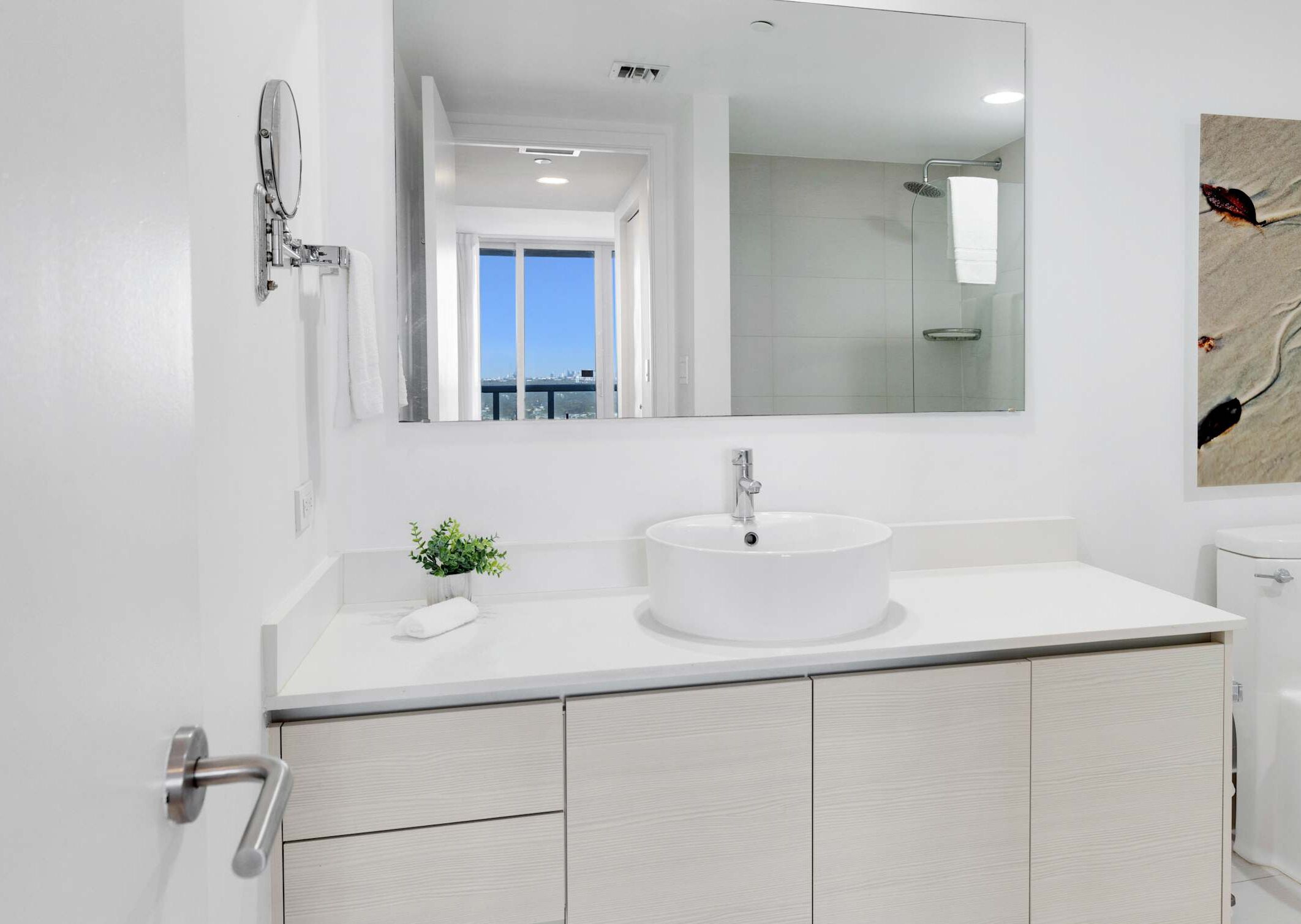 A modern bathroom with a large mirror, a round sink, and a shower.