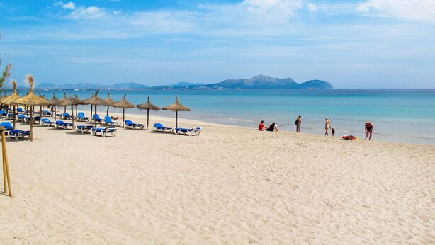 A beach with sun loungers and thatched umbrellas, a clear sky, and a calm sea. - De Vacances by Interhome (Son Serra Marina)