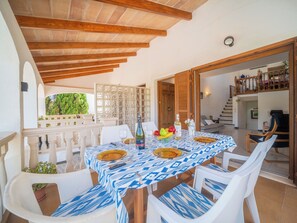 An outdoor dining area with a table set for four, surrounded by white chairs with patterned cushions. - De Vacances by Interhome (Son Serra Marina)