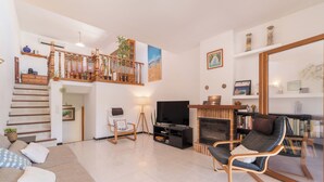 A spacious living area with a staircase, a fireplace, a TV, and a bookshelf. - De Vacances by Interhome (Son Serra Marina)