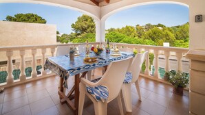 A covered outdoor dining area with a table set for two, surrounded by white chairs, and a view of greenery and buildings in the background. - De Vacances by Interhome (Son Serra Marina)