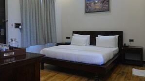 A neatly arranged hotel room with a large bed, a bedside table, a nightstand, a wooden dresser, and a painting on the wall. - GOLDEN CRESSIDA RESORT & PALACE (Mozamabad)