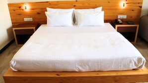A neatly made bed with white linens, a wooden headboard with two wall-mounted lights, and two bedside tables with a phone and a book on one. - GOLDEN CRESSIDA RESORT & PALACE (Mozamabad)
