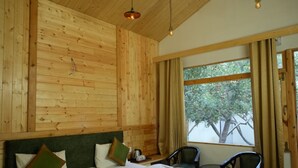 A wooden-paneled bedroom with a large bed, two chairs, a small table, and a window with curtains. - nine Apple Resort Dharali Harsil (Bhatwari)