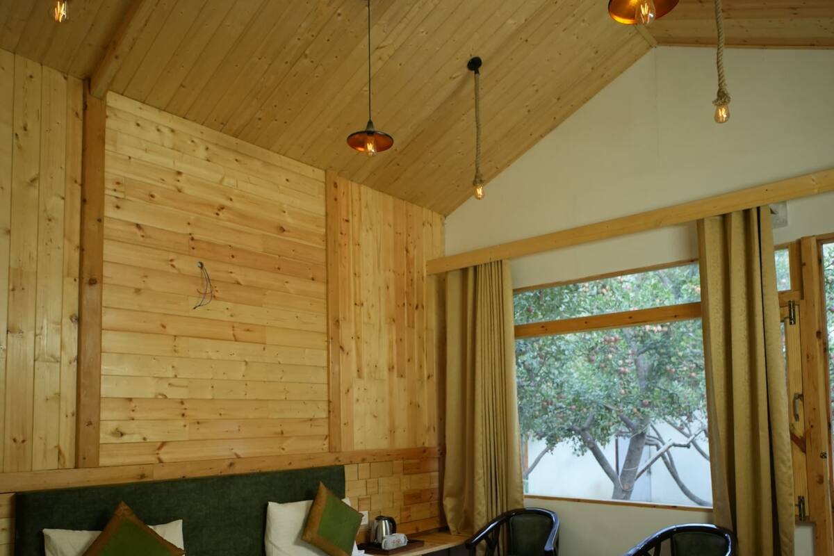 A wooden-paneled bedroom with a large bed, two chairs, a small table, and a window with curtains.
