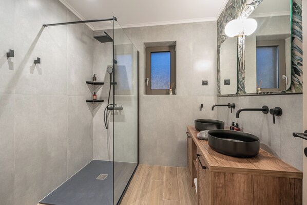 A modern bathroom with a glass-enclosed shower, a wooden vanity with a large basin, and a small window.