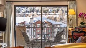 A hotel room with a balcony, a table, two chairs, a sofa, a TV, and a lamp.