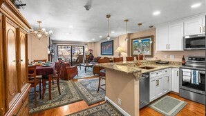 A spacious kitchen with a central island, white cabinetry, stainless steel appliances, and a dining area with a large window.