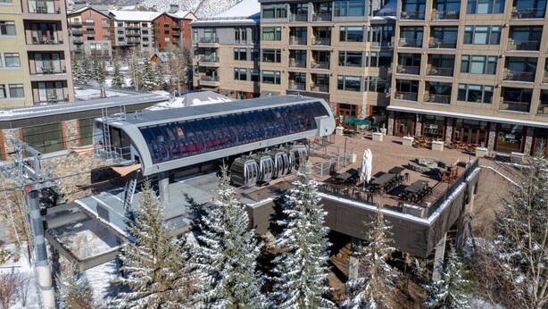 A modern hotel with multiple floors, outdoor seating areas, and a ski lift visible in the background.