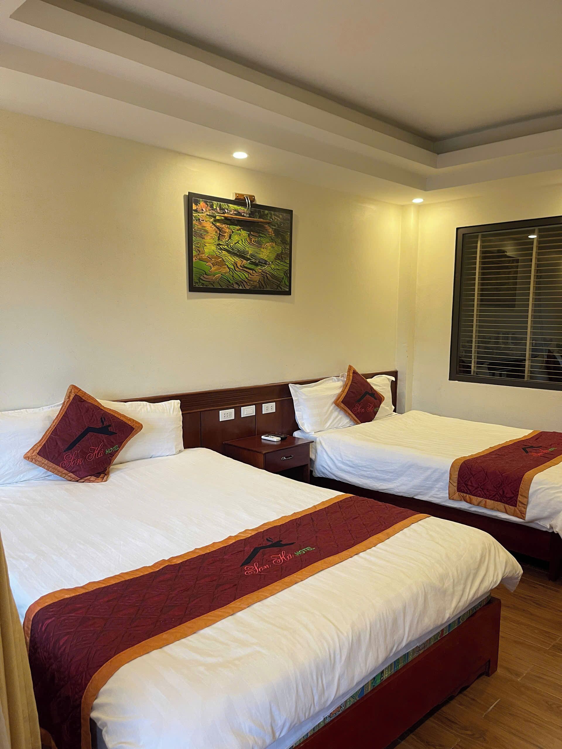 A hotel room with two beds, a nightstand, a painting on the wall, and a window with blinds.
