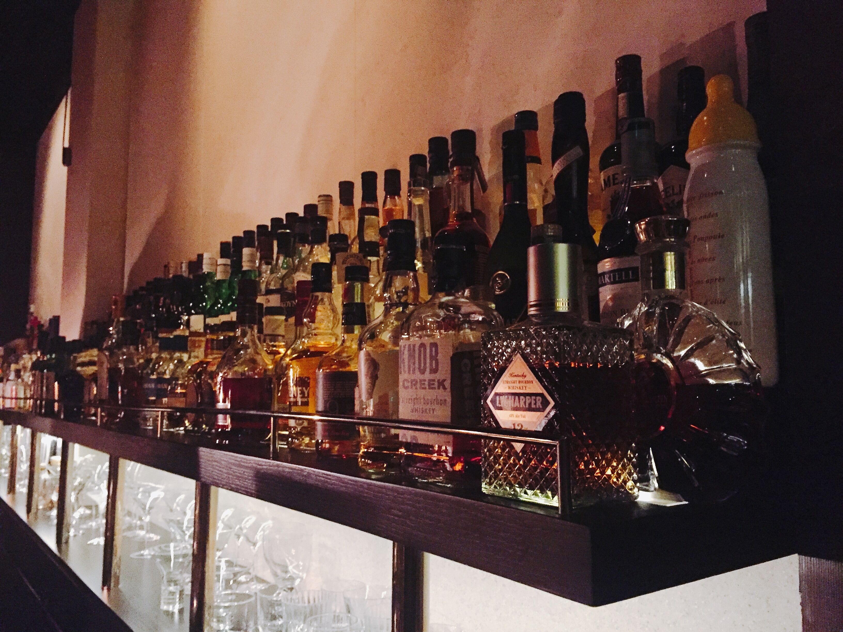 Un bar con diversas botellas de licores y copas a la vista.