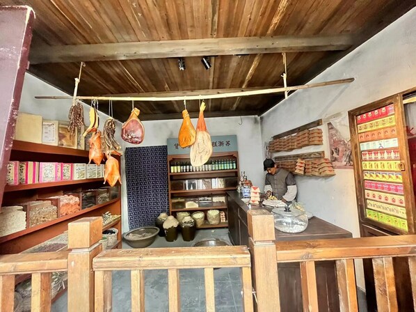 A rustic shop with hanging meats, shelves of packaged goods, and a counter with a person preparing food. - Jinglai Hotel Bushe (Shanghai)