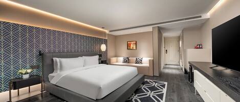 A modern hotel room with a large bed, a TV, a sofa, and a desk.