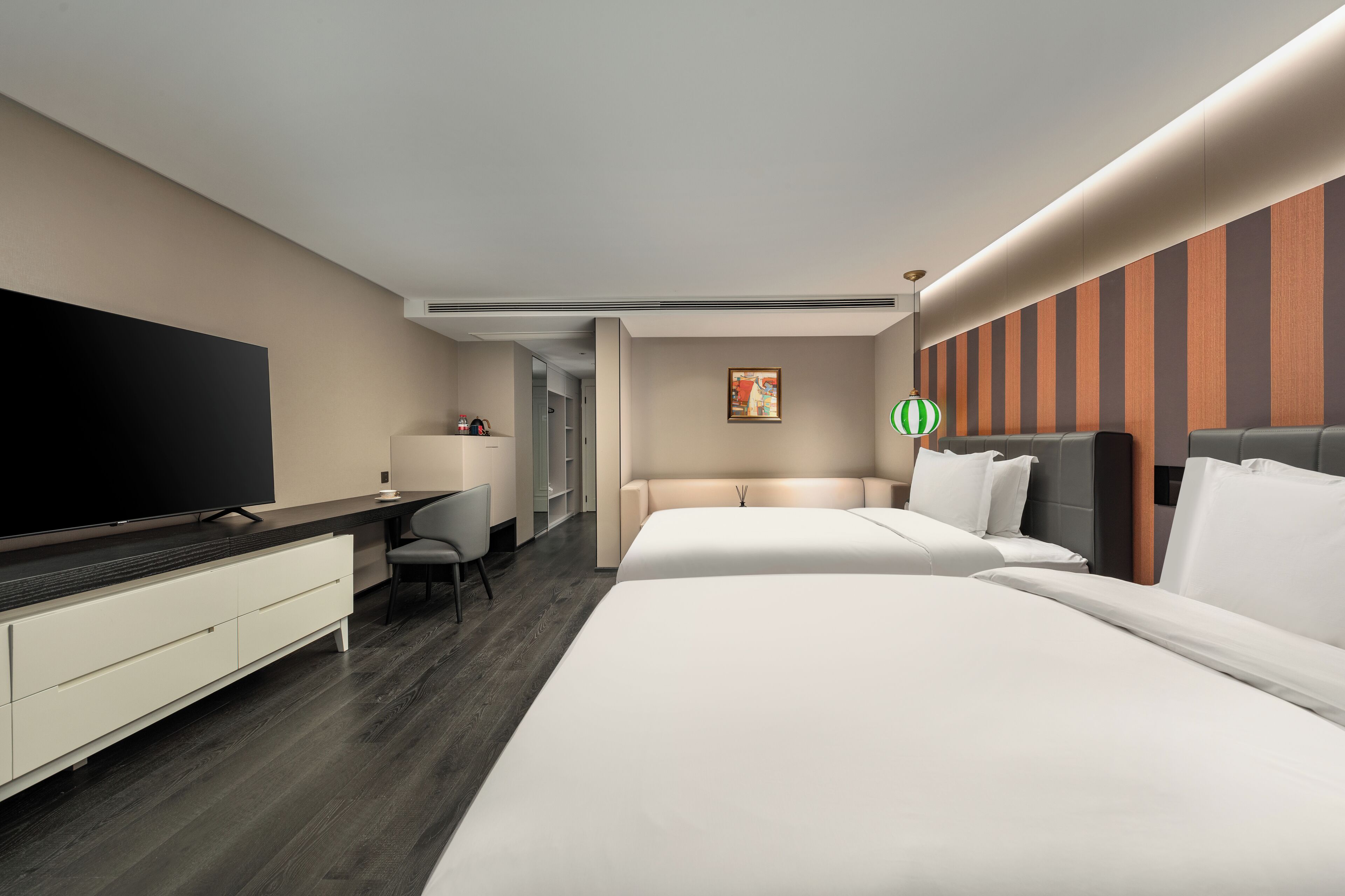 Een hotelkamer met een grote flatscreen-tv, een bureau met stoel, twee bedden en een gestreepte wand.