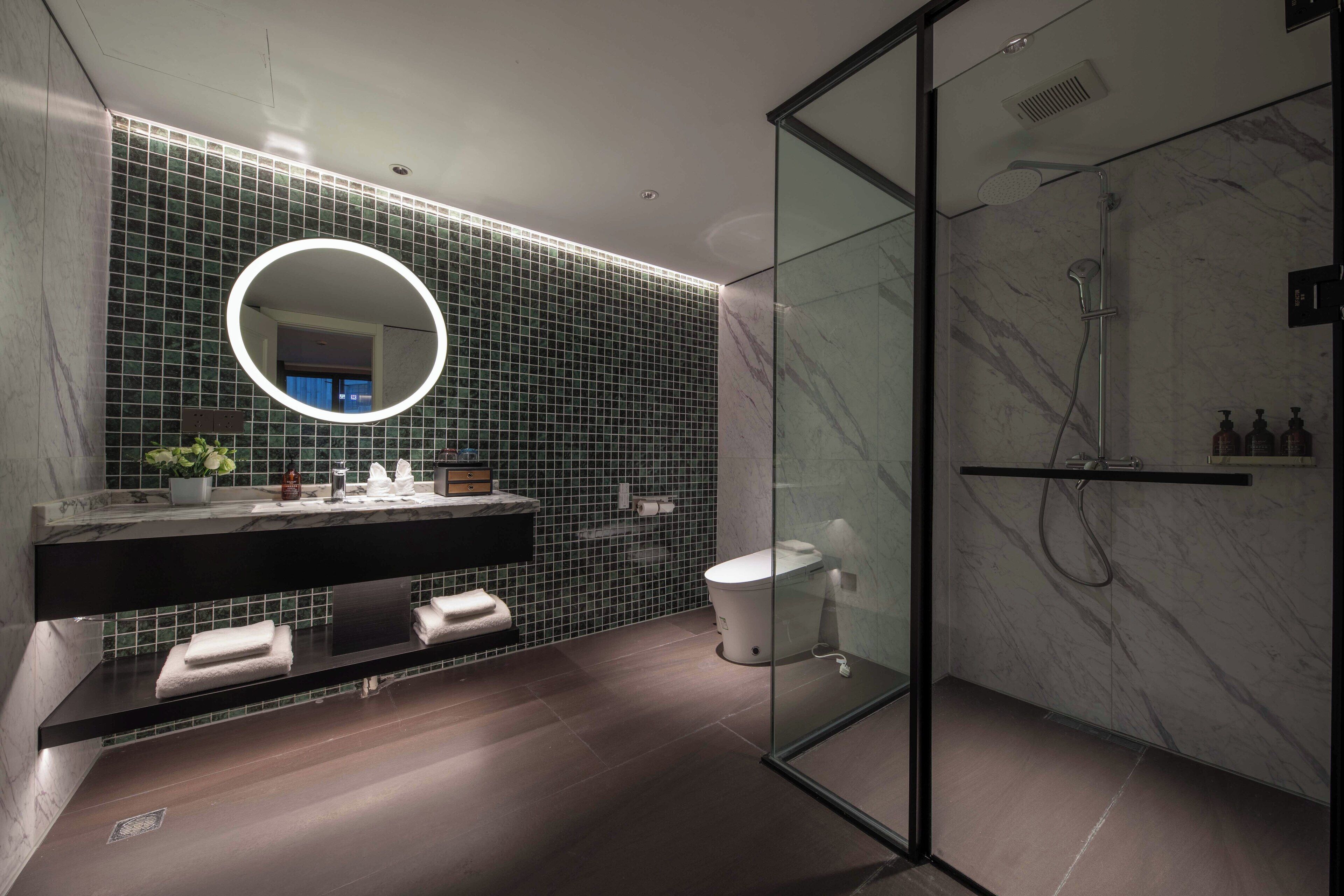 Un baño moderno con ducha de vidrio, un espejo redondo y suelo de madera oscura.