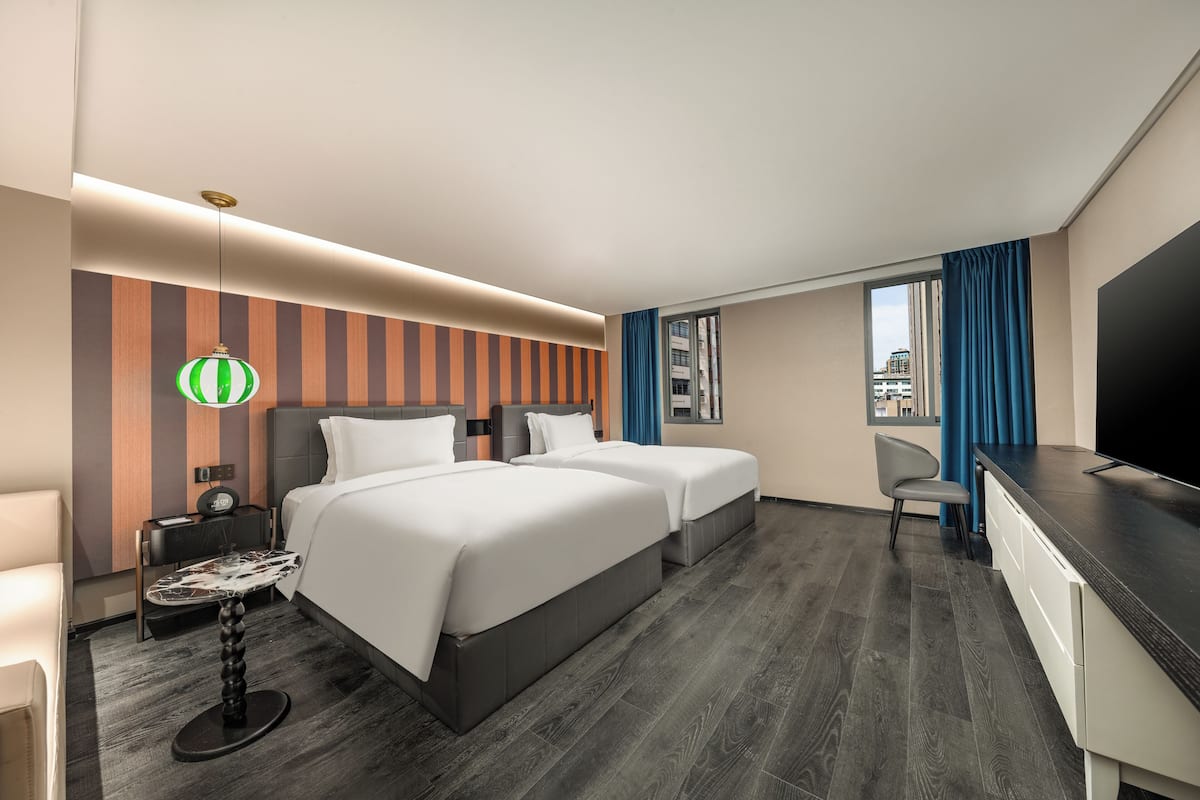 A hotel room with two beds, a desk, a chair, a TV, and a city view.