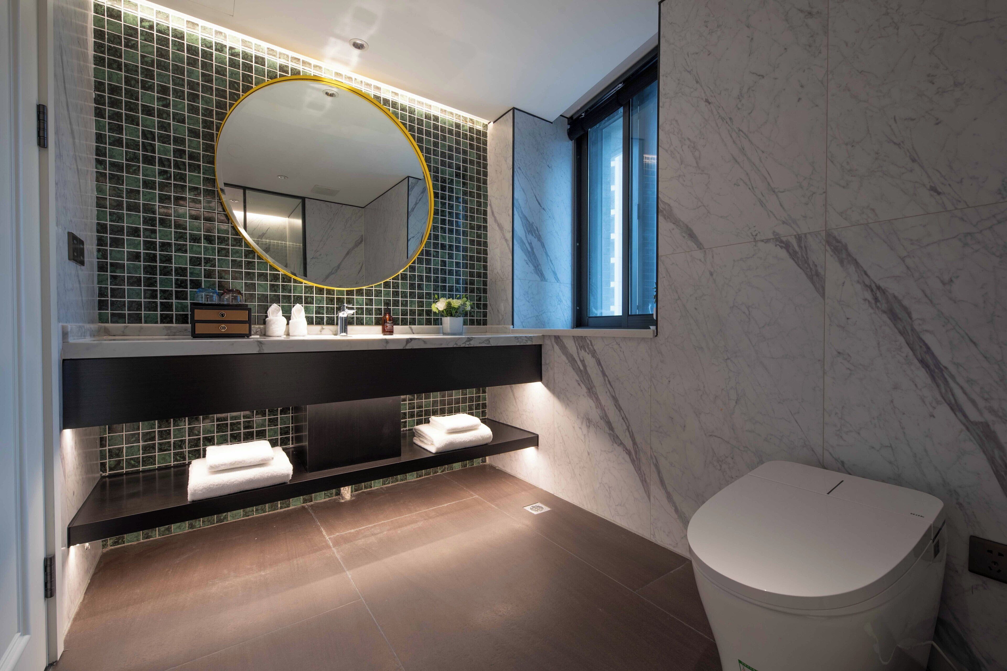 A modern bathroom with a large mirror, dark countertop, and a toilet.