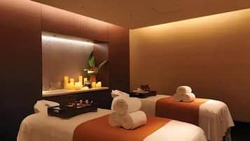 Two beds with white linens and brown headboards, a large mirror, and a minimalist design.
