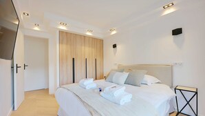 A modern bedroom with a large bed, white bedding, and a wooden wardrobe. - Charming Apt With AC & Balcony (Suresnes)