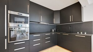 A modern kitchen with dark cabinetry, stainless steel appliances, and a view to an outdoor seating area. - Charming Apt With AC & Balcony (Suresnes)