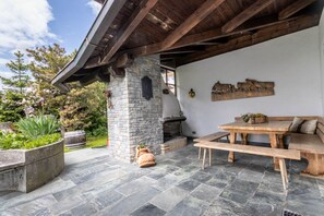 A stone fireplace, wooden bench, and outdoor dining table in a covered patio area.