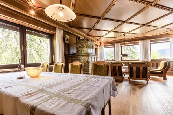A dining area with a table set for four, surrounded by wooden chairs, large windows with a view of greenery, and a decorative urn on the table.
