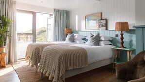 Un dormitorio con una cama grande, vistas al exterior, una mesita de noche con lámpara y una silla.