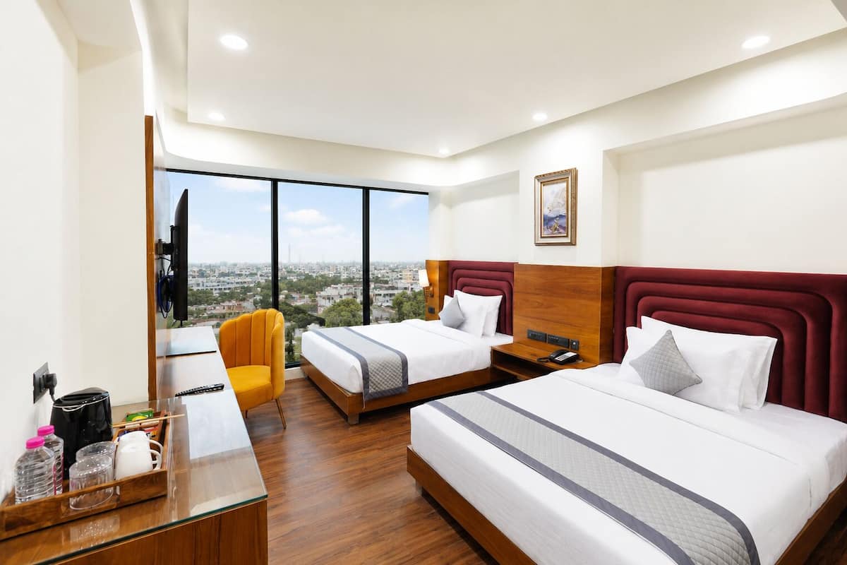 A hotel room with two beds, a desk, a chair, a TV, and a city view.