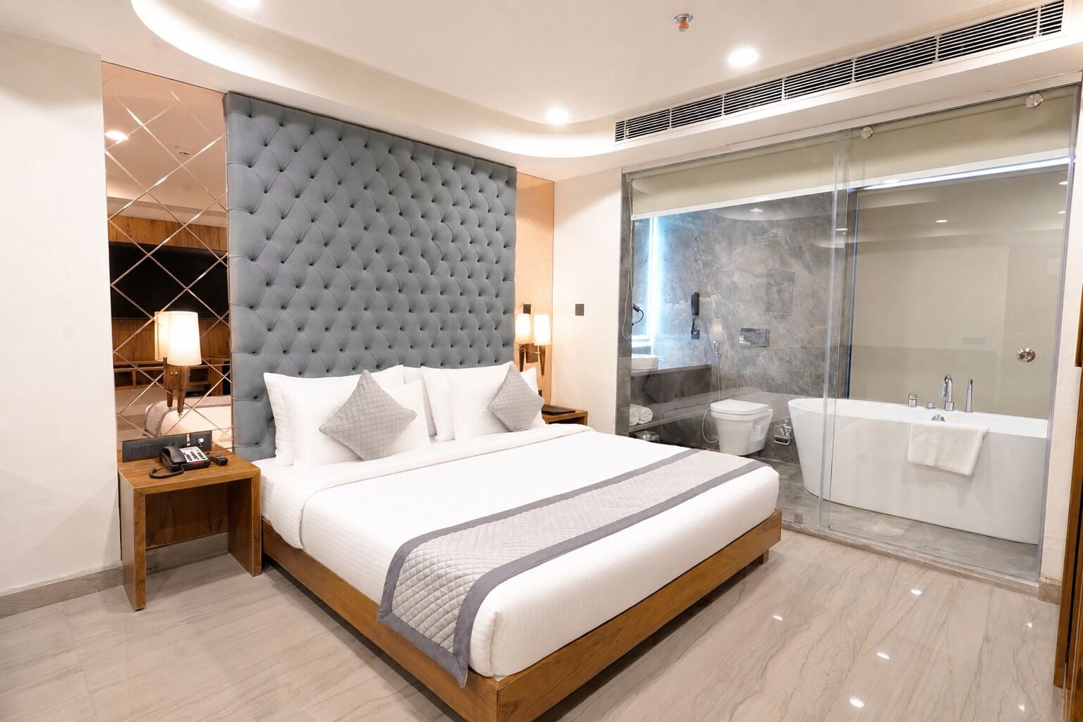A modern hotel room with a large bed, a separate bathroom, and a glass shower enclosure.