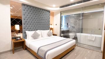 A modern hotel room with a large bed, a separate bathroom, and a glass shower enclosure.