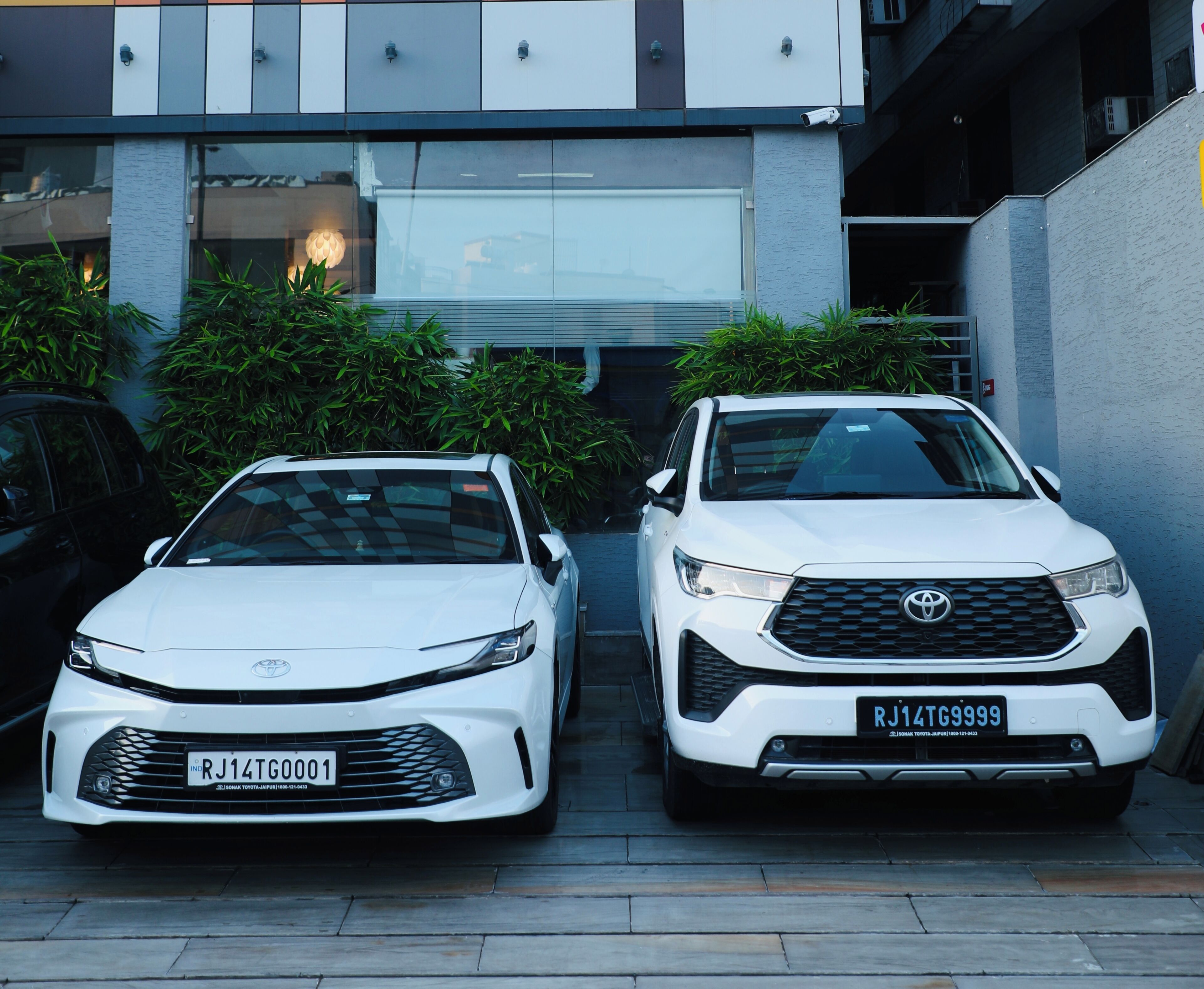 Dos camionetas Toyota SUV blancas estacionadas en una entrada con un edificio moderno al fondo.