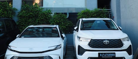 Dos camionetas Toyota SUV blancas estacionadas en una entrada con un edificio moderno al fondo.